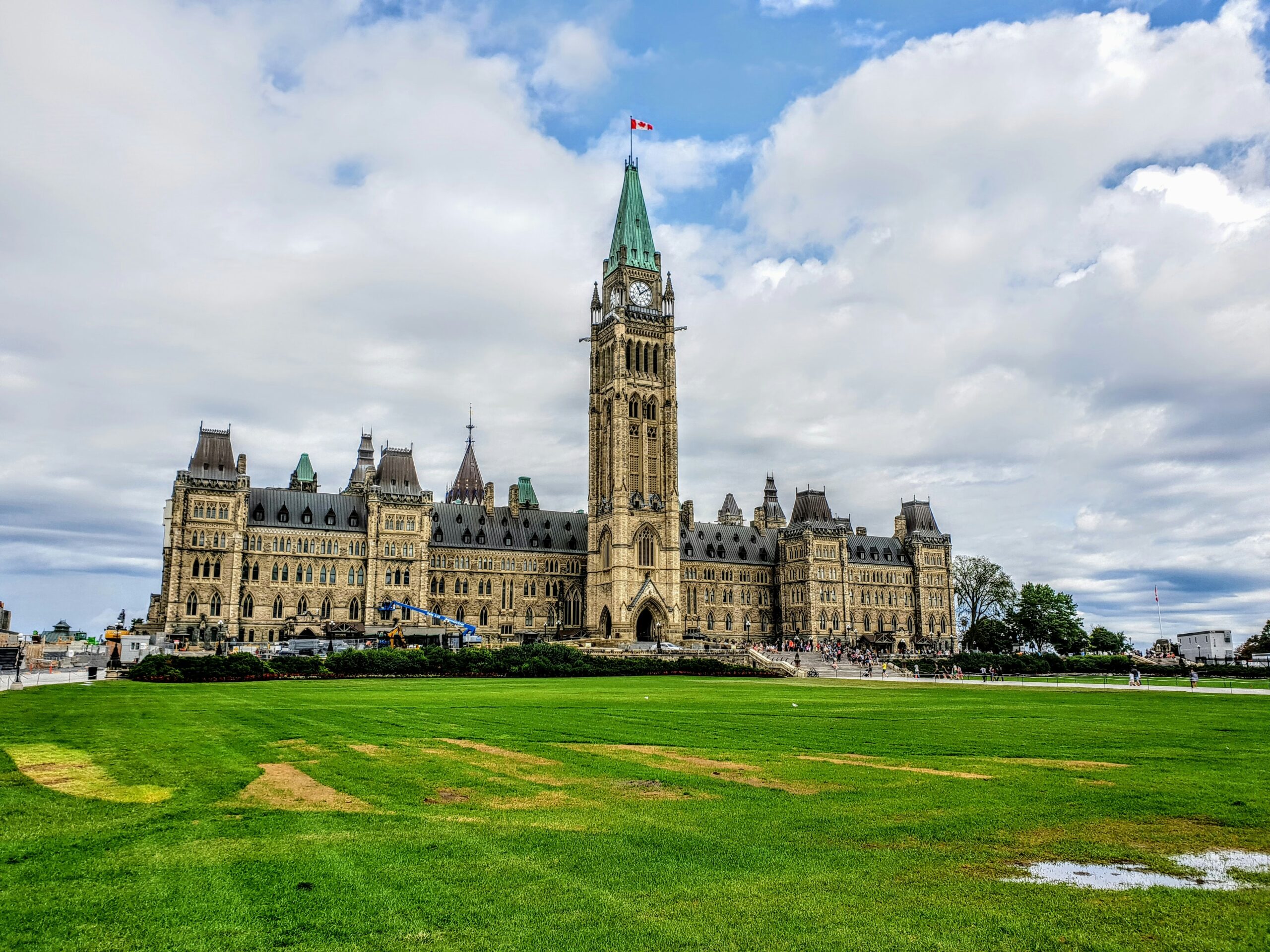 Parliament Hill in Ottawa with a green lawn in the foreground and the historic building under a cloudy sky, highlighting the city served by weed delivery and cannabis delivery.