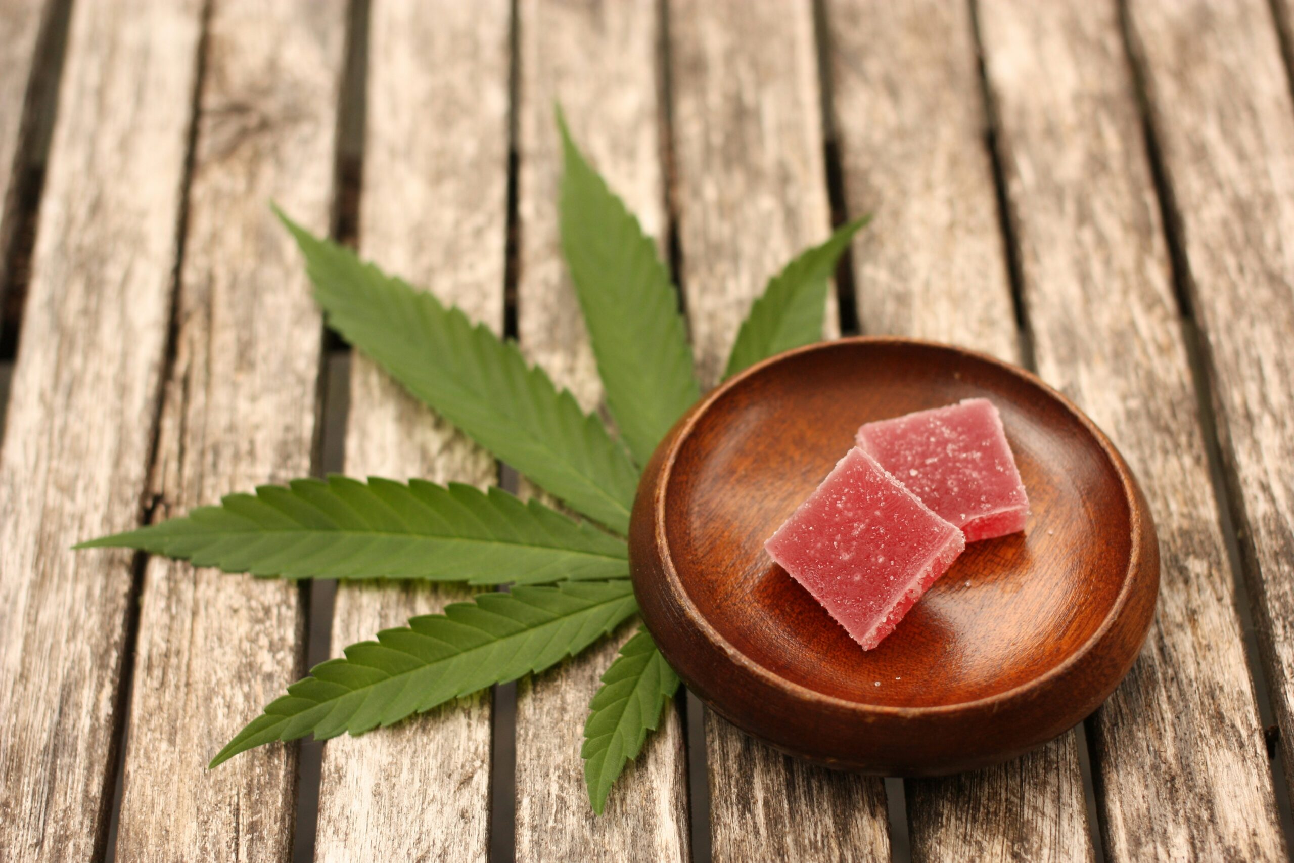 Two red cannabis edible gummies on a wooden dish, placed on a table with cannabis leaves, after a weed delivery and cannabis delivery from A1 Terps