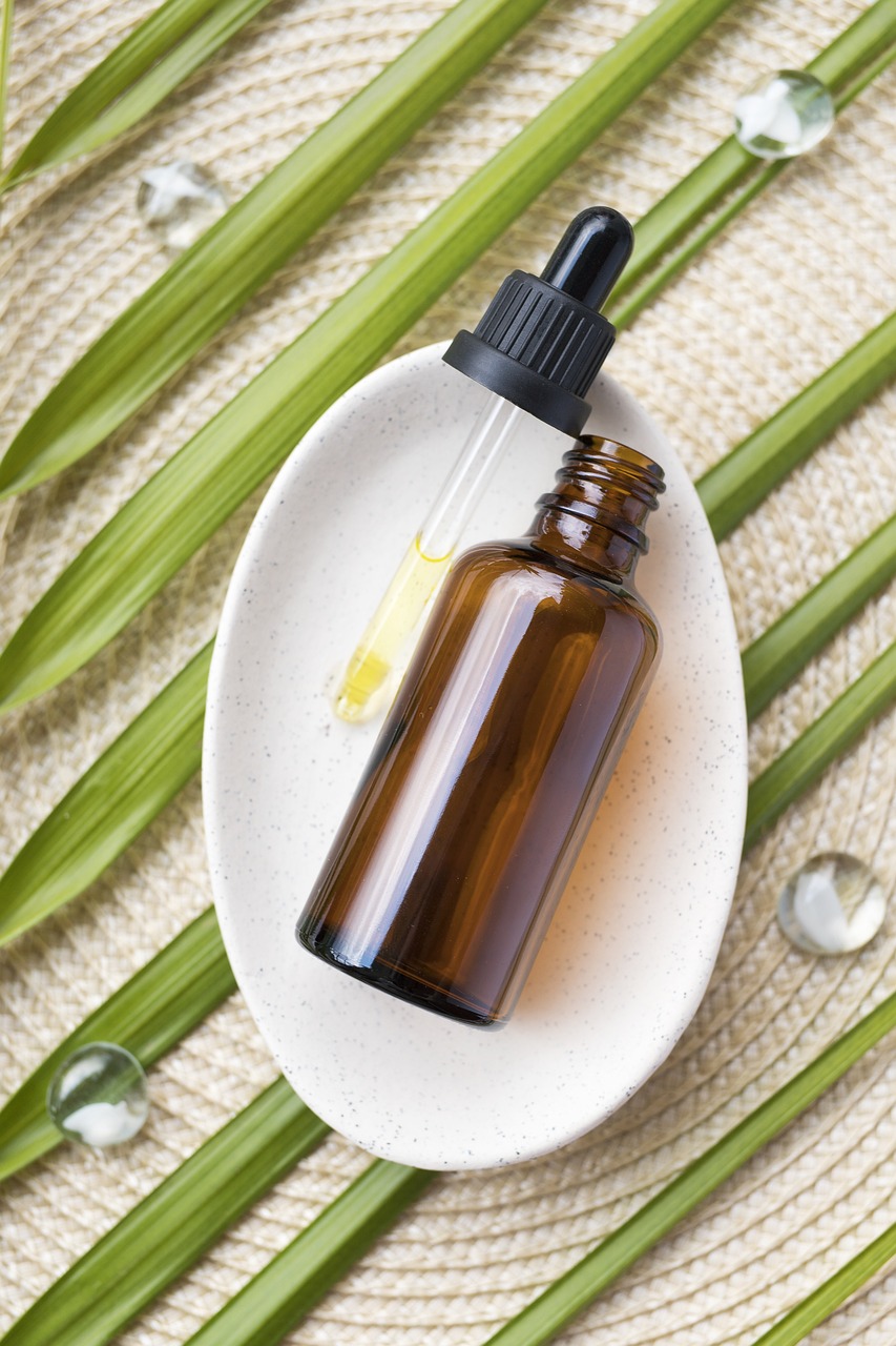 A small bottle of CBD oil for cannabis delivery with a dropper, placed on a white dish with green leaves in the background.