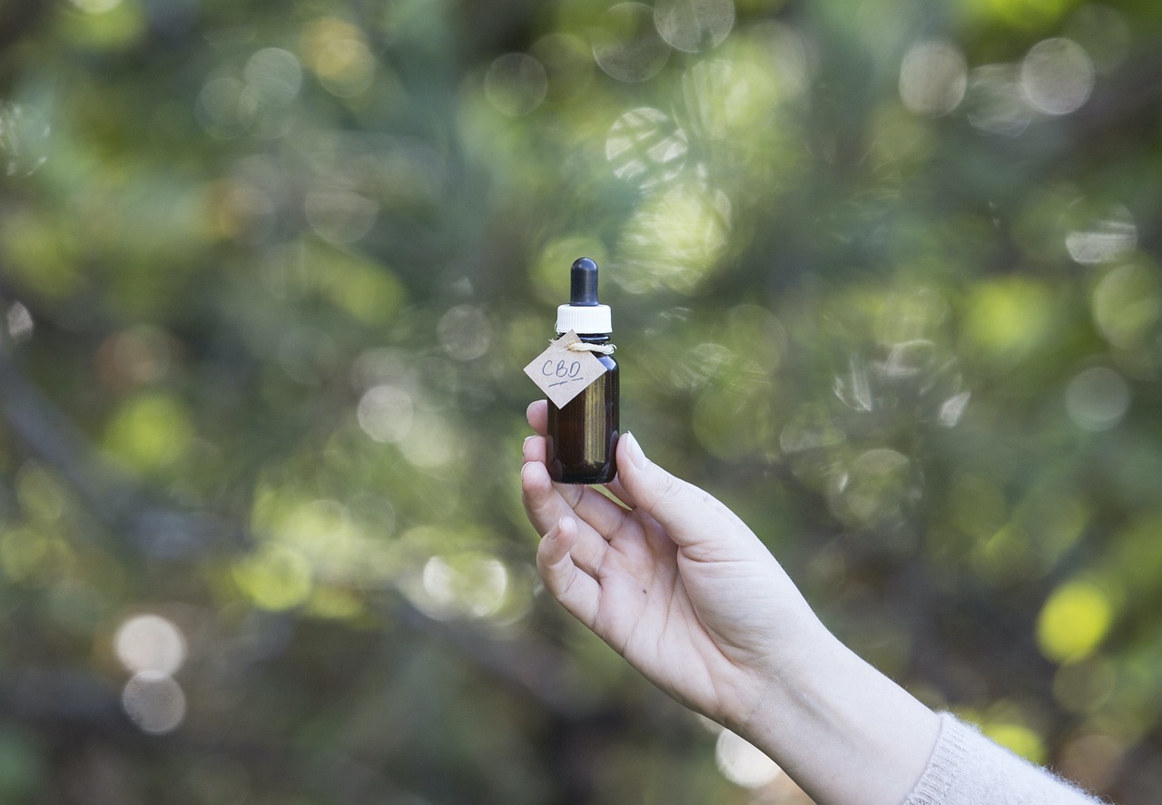 A hand holding a small bottle of CBD oil for weed delivery in a natural outdoor setting.
