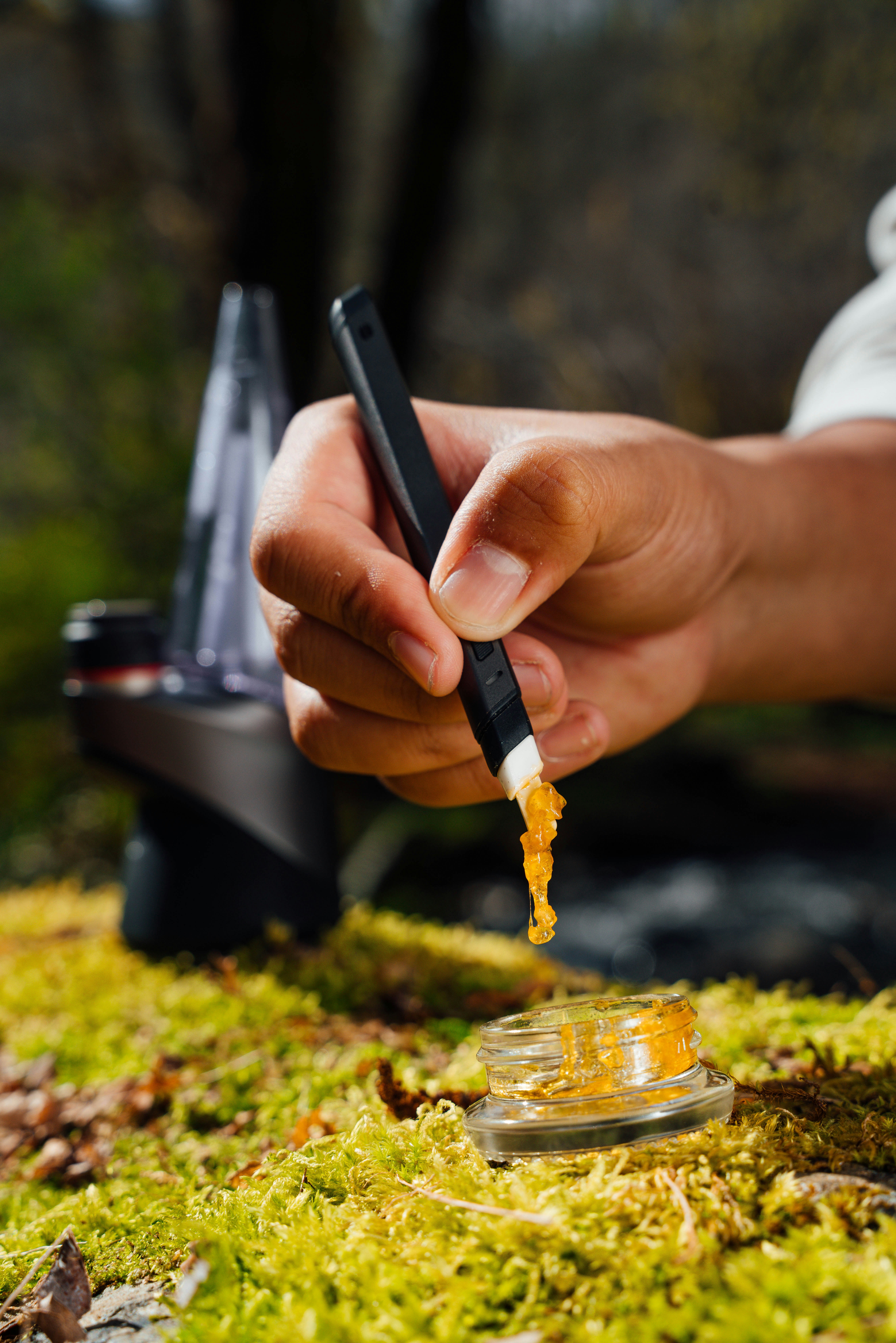 Hand holding a dab tool with cannabis concentrate over a glass container, ready for use.