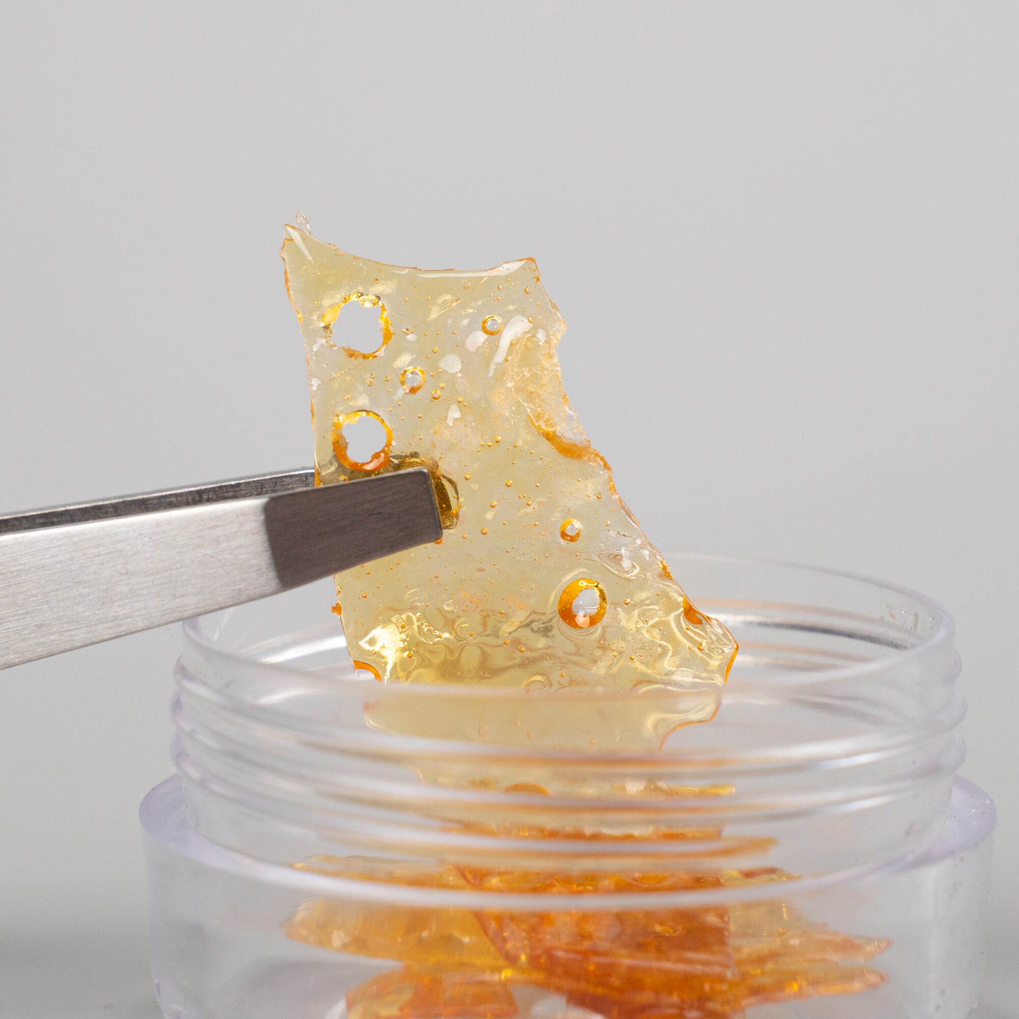 A slab of shatter cannabis concentrate being handled with tweezers.