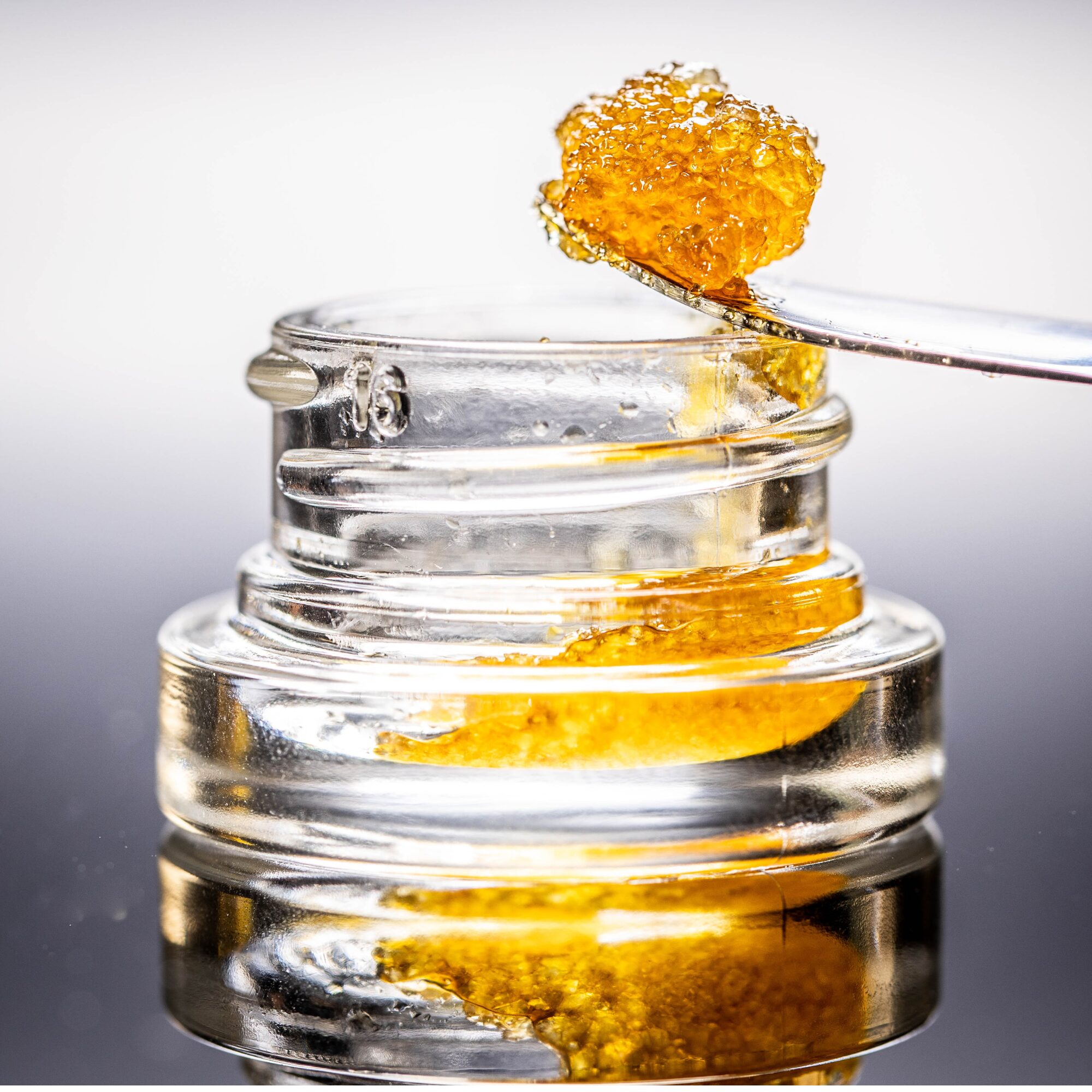 Close-up of diamond sauce THCA concentrate being scooped from a jar.